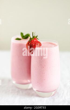 Two glasses of strawberry milkshake with mint and strawberry garnish on table. Stock Photo