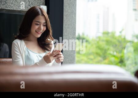 Cheerful young Asian woman using smartphone and receiving good news from the message on mobile chat application at coffee shop Stock Photo
