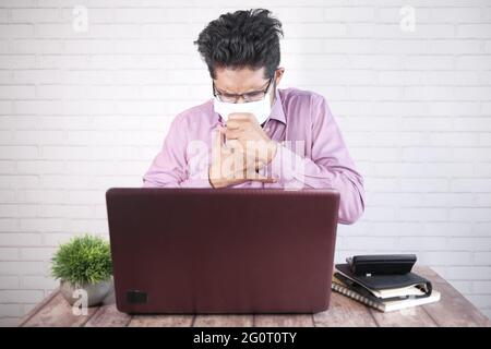 young asian man coughing and sneezes while sited on desk Stock Photo