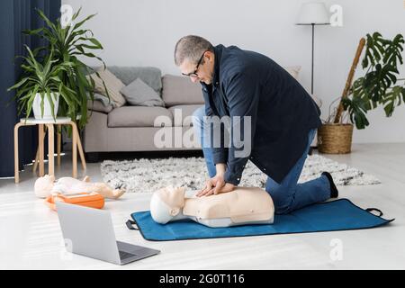 Paramedic demonstrating first aid on manikin during training alone in living room. The instructor showing CPR on training doll Stock Photo