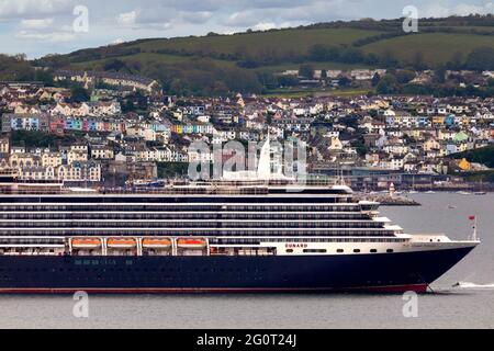 The huge Queen Victoria cruise ship is pictured anchored alongside the fishing port of Brixham, Devon. Stock Photo