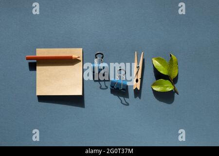 Notepad and colored pencil and clips and green leaf on desk. navy blue background. Work and study place. flat lay, top view, copy space Stock Photo