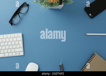 Glasses keyboard flower notepad mouse pen pencil and phone on blue background Stock Photo