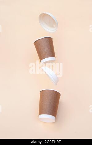 Brown sustainable paper coffee cups on a beige background with one of the cups flying. Zero waste concept. Stock Photo
