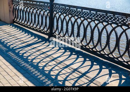 Shadows on a sunny day from the metal railings on the bridge over the river. Stock Photo