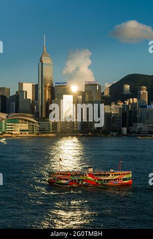 An iconic Star Ferry passes through the reflection of the late afternoon sun from the high-rise buildings of Wan Chai, Victoria Harbour, Hong Kong Stock Photo