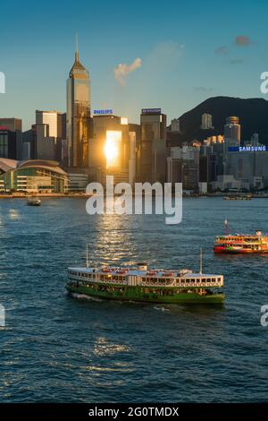 An iconic Star Ferry passes through the reflection of the late afternoon sun from the high-rise buildings of Wan Chai, Victoria Harbour, Hong Kong Stock Photo