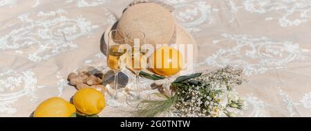 Horizontal banner or header with two white wine glasses on a blanket with flowers, a straw hat and tropical fruits around. Stock Photo