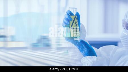 Composition of female scientist in ppe suit holding beaker with biohazard symbol with copy space Stock Photo