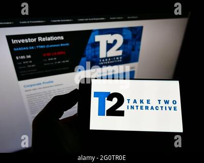 Person holding mobile phone with logo of video game company Take-Two Interactive Software Inc. on screen in front of webpage. Focus on phone display. Stock Photo