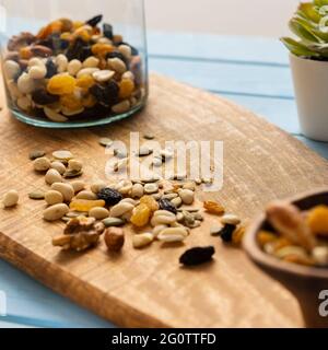 A mixture of loose nuts. Storage of nuts in a glass jar, on a wooden table. Scattered carelessly on the cutting board. Light snack. Stock Photo