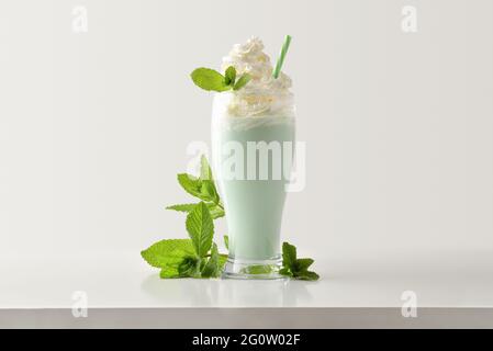 Mint milkshake with cream decorated with leaves around on white wooden table and light isolated background. Front view. Stock Photo