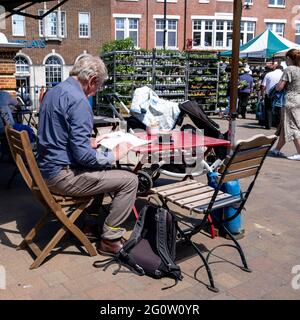 Epsom Surrey London UK, June 03 2021, A Single Senior Or Elderly Man Sitting At an Outdoor Table Reading And Drinking Coffee Alone Stock Photo