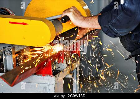 Metal sawing in the workshop at the production site with a stationary machine. Electric circular saw for metal. The worker cuts the metal profile and sparks fly. Close-up. Stock Photo