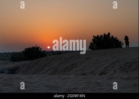 Female tourist taking picture of Sunrise at Thar desert, Rajasthan India with desert plants in frame. Stock Photo