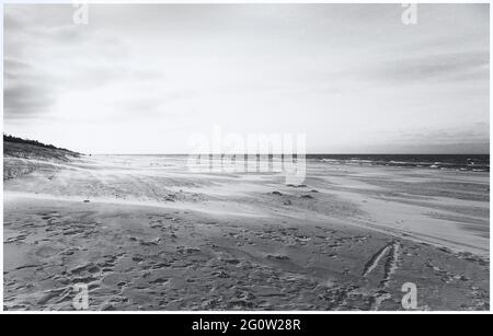 Fishing boats on the coast of the Osstsee on the beach in Poland in a melancholic black and white look. Beach on the Baltic Sea with many footprints. Stock Photo