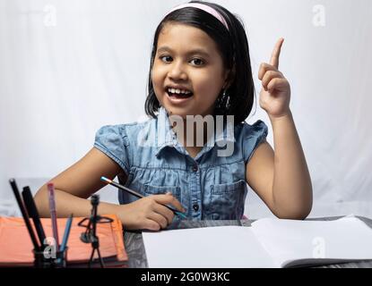 A pretty Indian girl child thinking and looking at camera while studying with smiling face Stock Photo