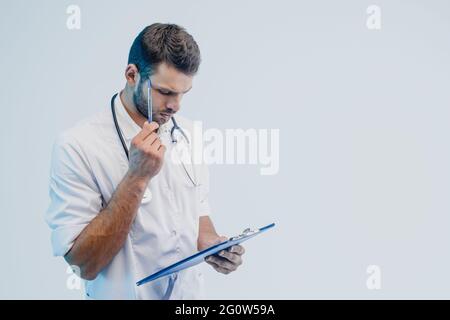Thoughtful male doctor read something in clipboard Stock Photo