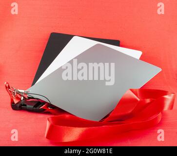 Gray cards for photographers placed on a red background. There are three cards, one gray, one white and one black. They are attached with a hook and a Stock Photo