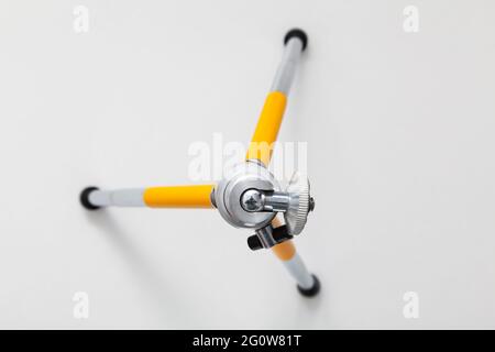 Small tripod with yellow extendable legs planted on a white background. The tripod is seen from above. The top is in focus and the base of the legs is Stock Photo