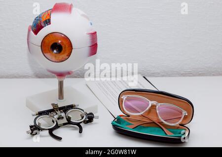 On a table there is a model of an eye, some glasses to graduate the vision, some new glasses in their case and a reading letter Stock Photo