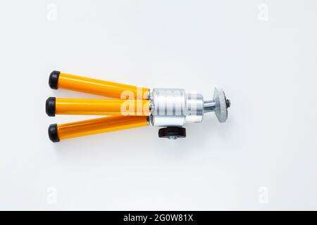 Small folded tripod with yellow legs lying on a white background. The base of the legs is made of black rubber. Stock Photo