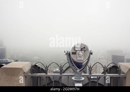 Binoculars on skyscraper deck in foggy modern city Stock Photo
