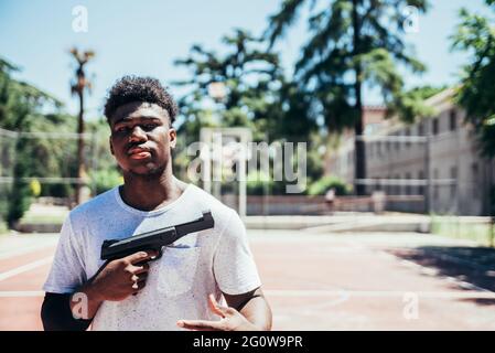 Black African American boy clutching a gun on an urban basketball court. Stock Photo