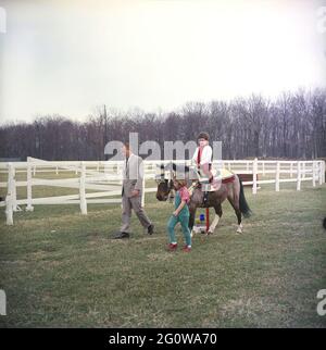 KN-C27667  31 March 1963  Weekend at Camp David. Sally Fay riding horse 'Macaroni' lead by Paul 'Red' Fay and Caroline Kennedy. 'Macaroni' wears a Moroccan saddle given to the Kennedy's by King Hassan II of Morocco. Camp David, Maryland.  Please credit 'Robert Knudsen. White House Photographs. John F. Kennedy Presidential Library and Museum, Boston' Stock Photo