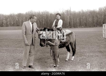 KN-27637  31 March 1963  Sally Fay riding horse 'Macaroni' lead by Paul 'Red' Fay and Caroline Kennedy. 'Macaroni' wears a Moroccan saddle given to the Kennedy's by King Hassan II of Morocco. Camp David, Maryland.  Please credit 'Robert Knudsen. White House Photographs. John F. Kennedy Presidential Library and Museum, Boston' Stock Photo