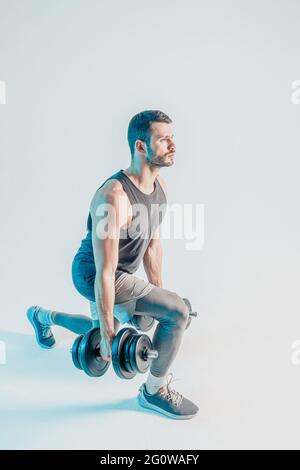 Serious young man doing lunges with dumbbells Stock Photo