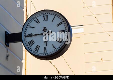 Street clock on the wall of the house. Classic dial with Roman numerals. Stock Photo
