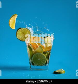 Flying slices of lime and orange in a refreshing summer lemonade, in a glass with large splashes of water on a light blue background. Colorful, summer Stock Photo