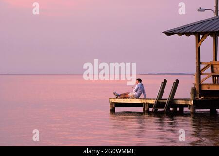 A young man reclines on a Fairhope, AL, USA, municipal pier as the sun sets on Mobile Bay on Nov. 4, 2020. Stock Photo