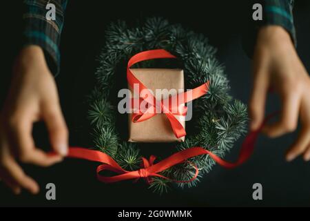 Woman making christmas wreath with pine tree and red ribbon. Ideas for christmas decoriation. Christmas background. Stock Photo