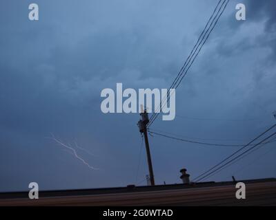 Dark storm clouds over the New Jersey shoreline with a small lightning burst near an electric pole line. Extremely dark clouds over the Atlantic. Stock Photo