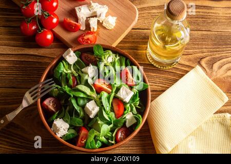 Salad of mung bean lettuce leaves, cheese, cherry, in a ceramic bowl on a wooden board. (Valerianella locusta). Diet and healthy food concept. Fogerls Stock Photo