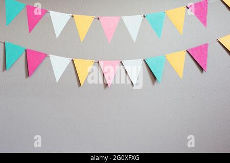 Colorful party flags over cement concrete gray wall texture background, pastel birthday colored flags with copy space Holiday concept Stock Photo