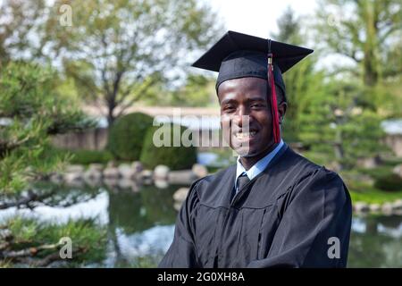 Handsome young black college graduate wearing cap and gown smiling proudly Stock Photo