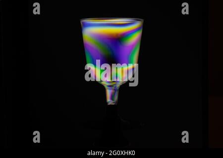 Transparent hovering plastic cup, polarized rainbow colored isolated on black background. Synthwave modern futuristic look. Stock Photo