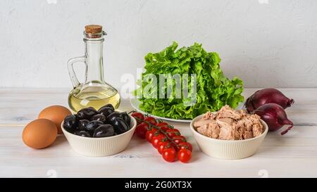 Ingredients for tasty tuna salad: canned tuna meat, fresh lettuce, boiled eggs, cherry tomatoes on the vine, black olives, red onion and olive oil. Stock Photo