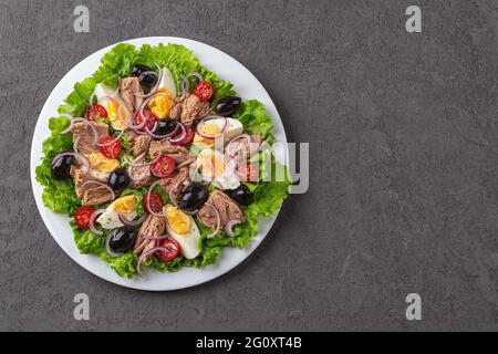 Tasty tuna salad on a white plate over dark textured surface. Mediterranean tuna salad with eggs and fresh vegetables. Low calories healthy eating. Stock Photo