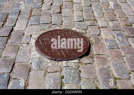 iron rusty manhole cover on an old cobblestone road on a sunny day on an old city road. Stock Photo
