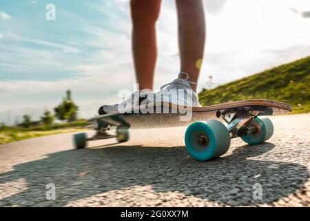 Wide angle legs on a longboard in motion at sunny day on the asphalt road. Close up of a spinning wheel. Stock Photo