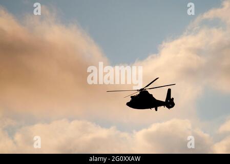 A U.S. Coast Guard helicopter in silhouette against a cloudy sky flies above a public beach on Dauphin Island, AL, USA, on Oct. 24, 2020. Stock Photo