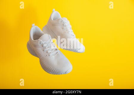 Levitation white sport shoes footwear on yellow wall. White sneakers shoes fly on yellow color background with copy space. Pair of sport male sneakers Stock Photo