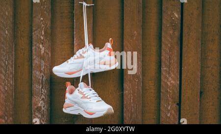 White womens sneakers with coral inserts hanging on nail on brown rustic wooden wall of planks. Banner Stock Photo