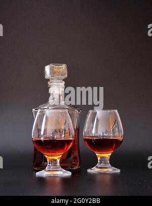 Two glasses half filled with cognac and a glass bottle with an alcoholic drink on a black background. Close-up. Stock Photo