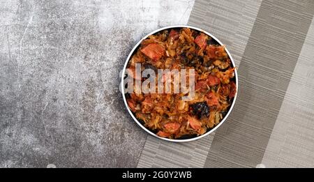 Bigos - traditional polish dish of stewed sauerkraut with prunes and sausages on a round plate on a dark gray background. Top view, flat lay Stock Photo