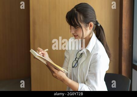 Side view of young female student looking on her notebook while doing assignment in library Stock Photo